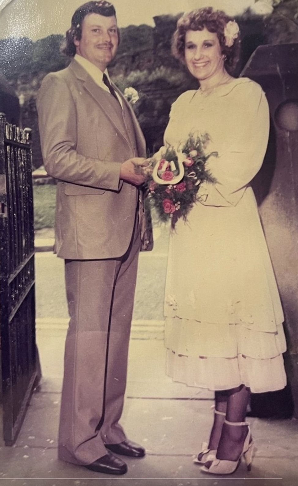 The founder's mum and dad on their wedding day, standing together at a church gate